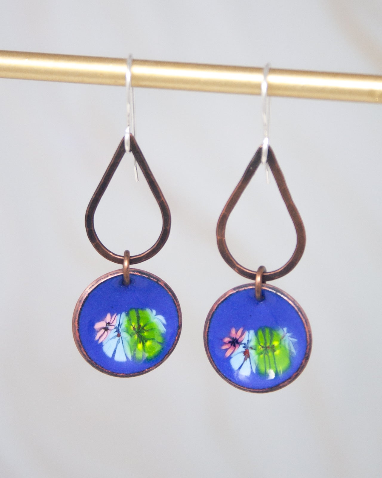 A pair of earrings with a blue circular pendant featuring a floral design.
