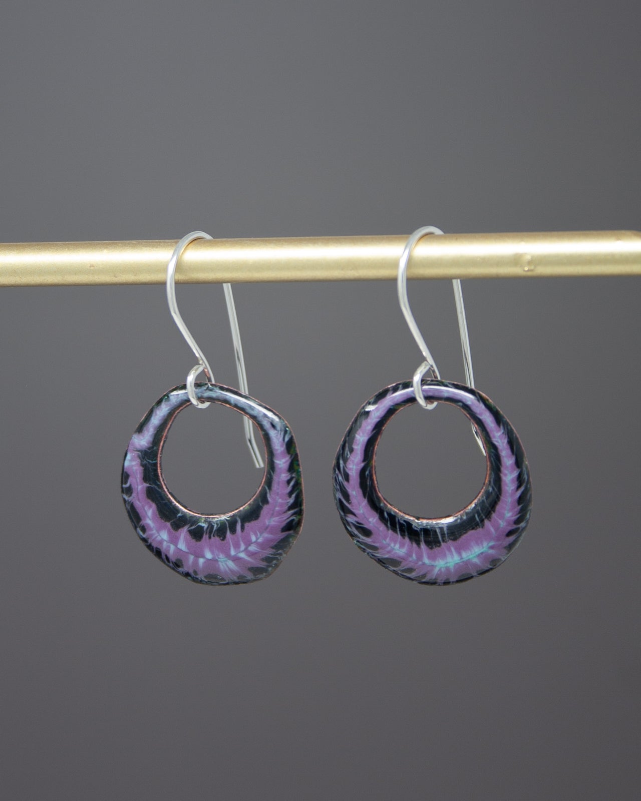 A pair of earrings with a black and purple design hanging from a gold bar.