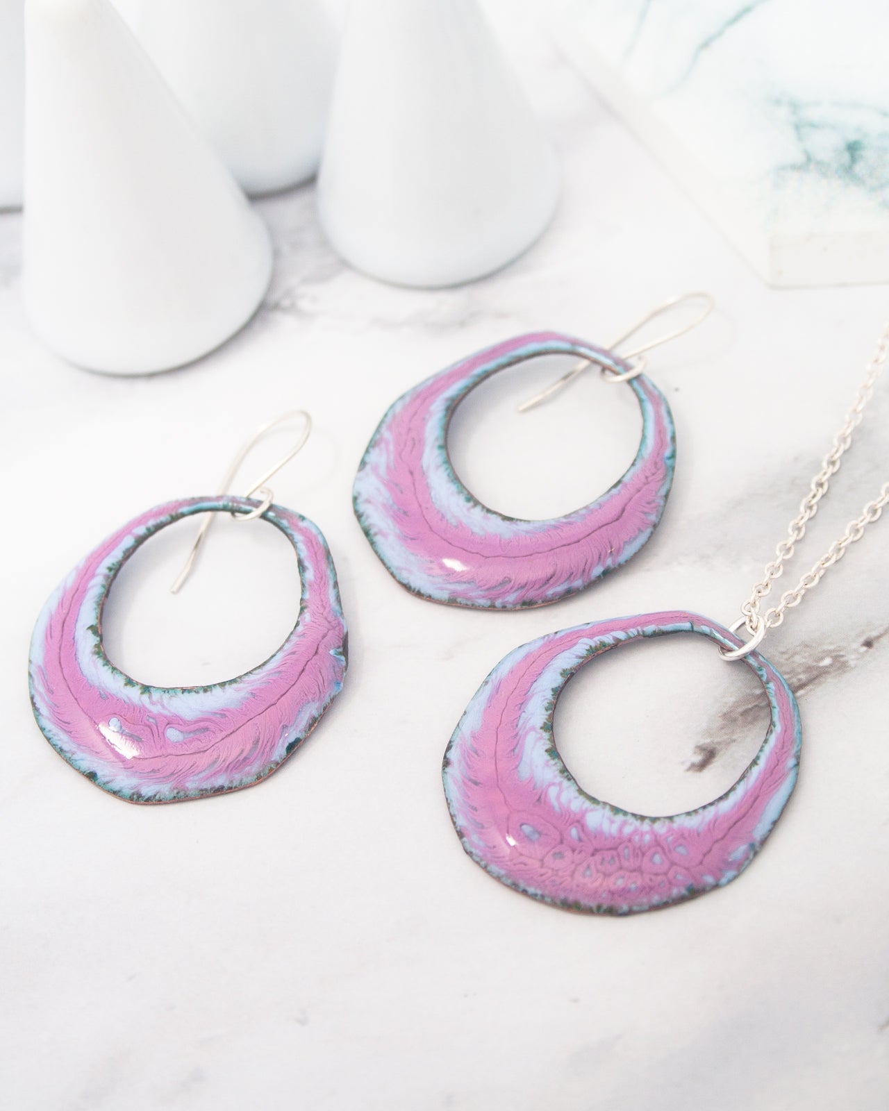 a pair of earrings and a necklace with a pink and blue color scheme, placed on a marble surface.