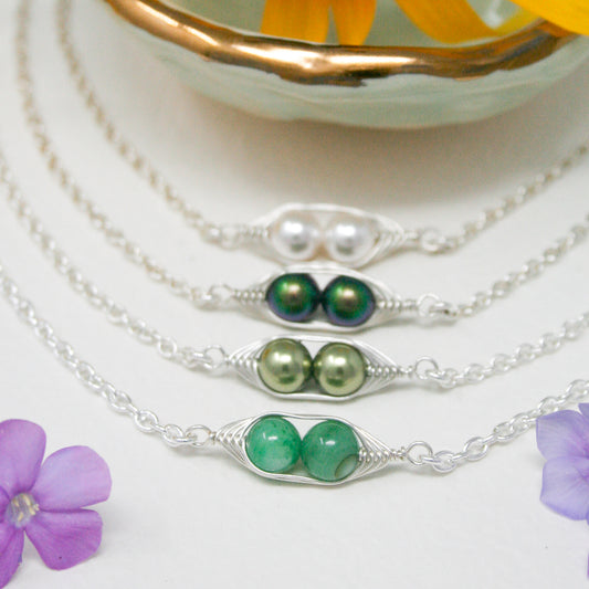 A collection of silver necklaces with various colored beads, including green, silver, and white pearls, arranged in a row on a white surface.