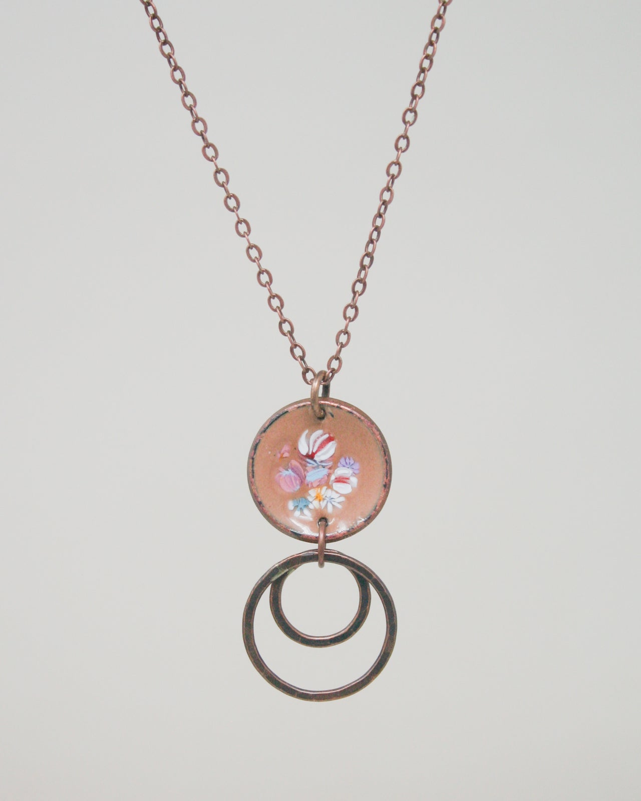 A necklace with a circular pendant featuring a floral design and two circular rings hanging from it.