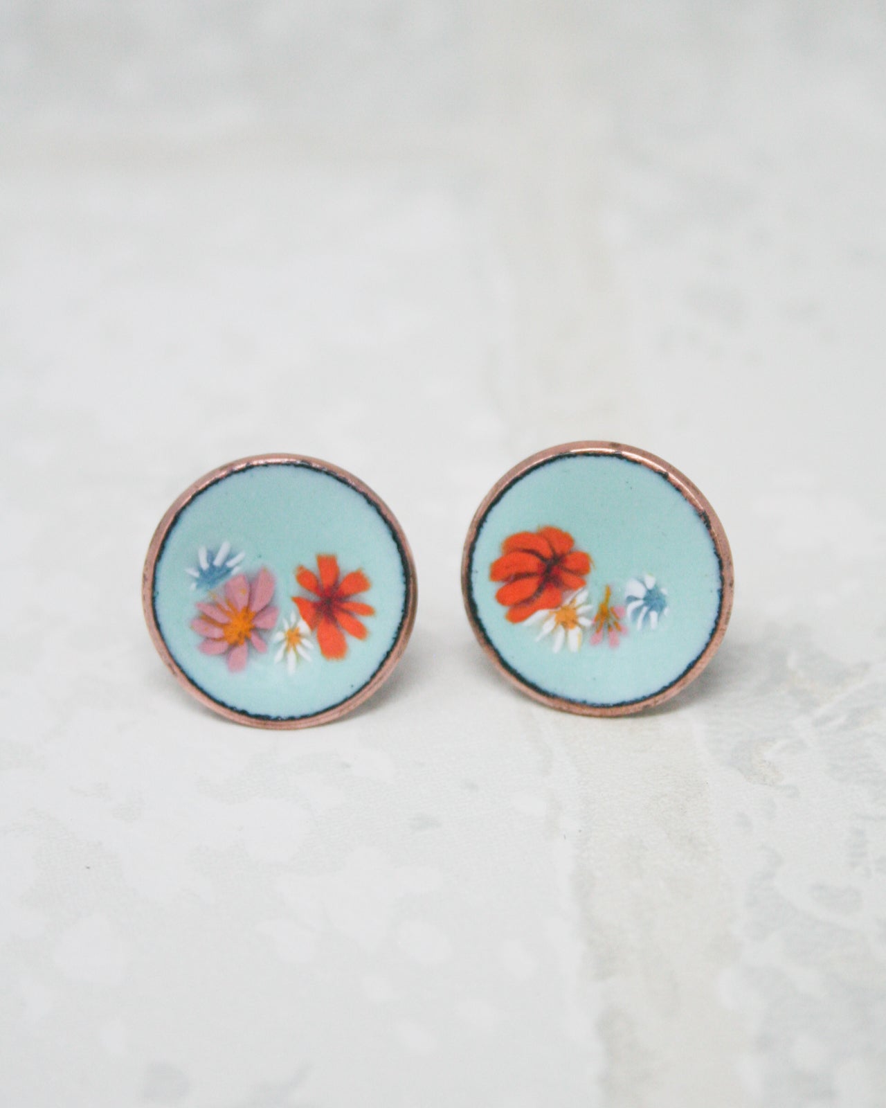 two circular earrings with floral designs on them, placed on a white surface.