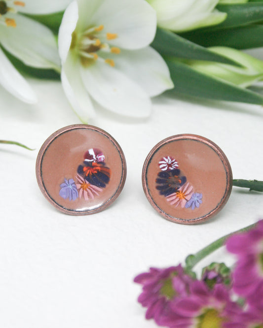 a close up of a pair of earrings with flowers in the background