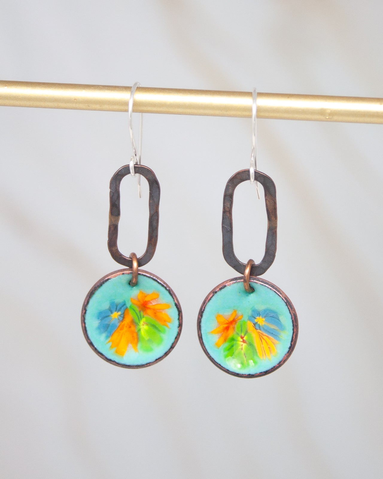 A pair of earrings with a circular design featuring a vibrant floral pattern in shades of blue, orange, and green.