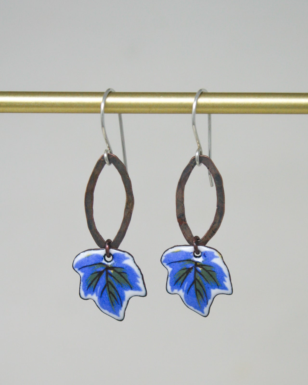A pair of earrings with leaf-shaped pendants hanging from a gold-colored metal hook.