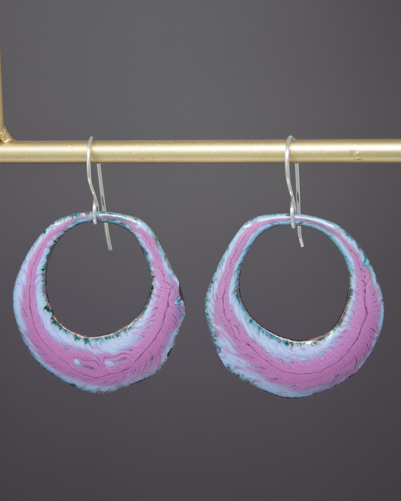 A pair of colorful earrings with a pink and blue color scheme, hanging from a gold-colored metal bar.
