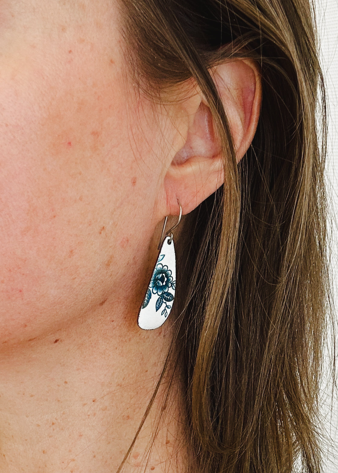 A close-up view of a person's ear wearing a pair of earrings with a floral design.