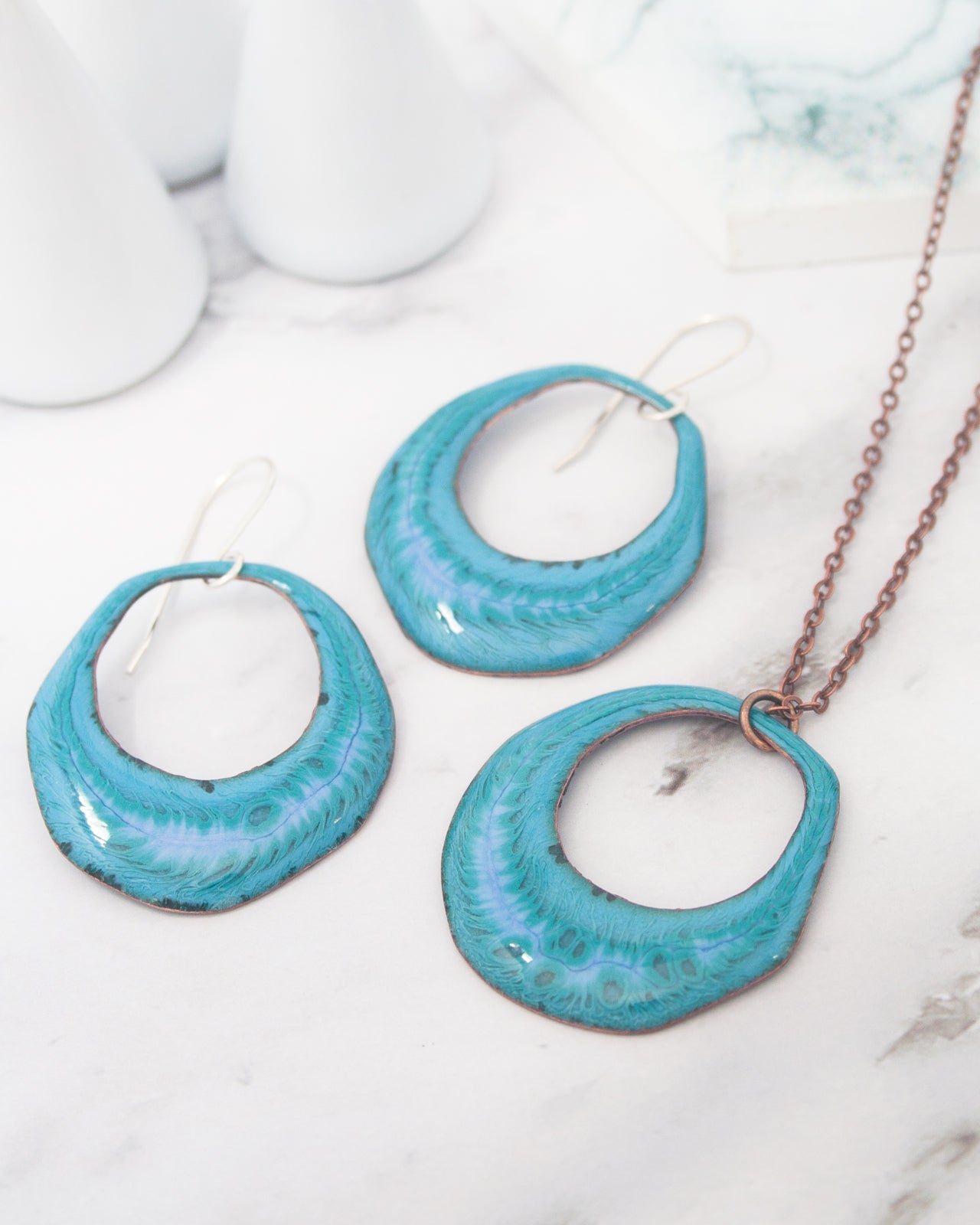 a necklace and earrings with turquoise-colored metal, placed on a marble surface.