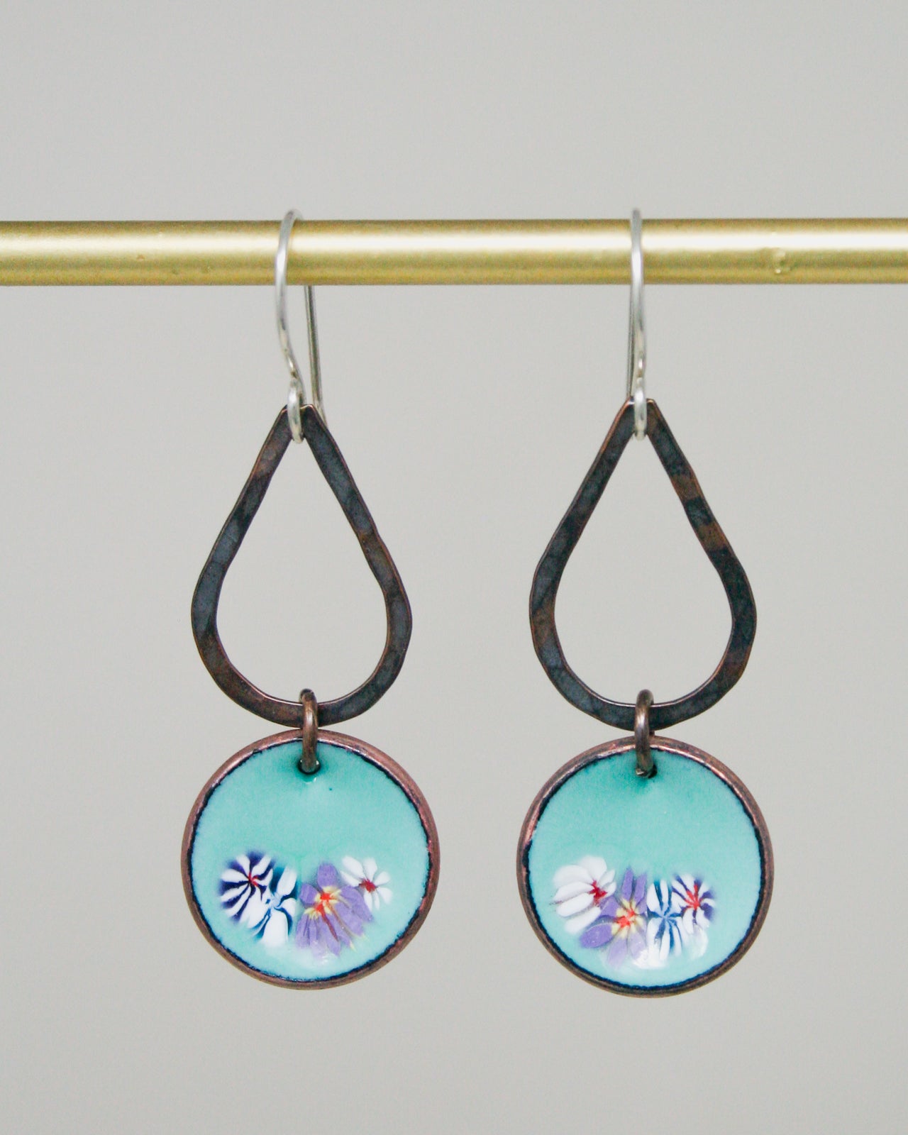 A pair of earrings with a teardrop-shaped design and a circular pendant featuring a floral pattern.