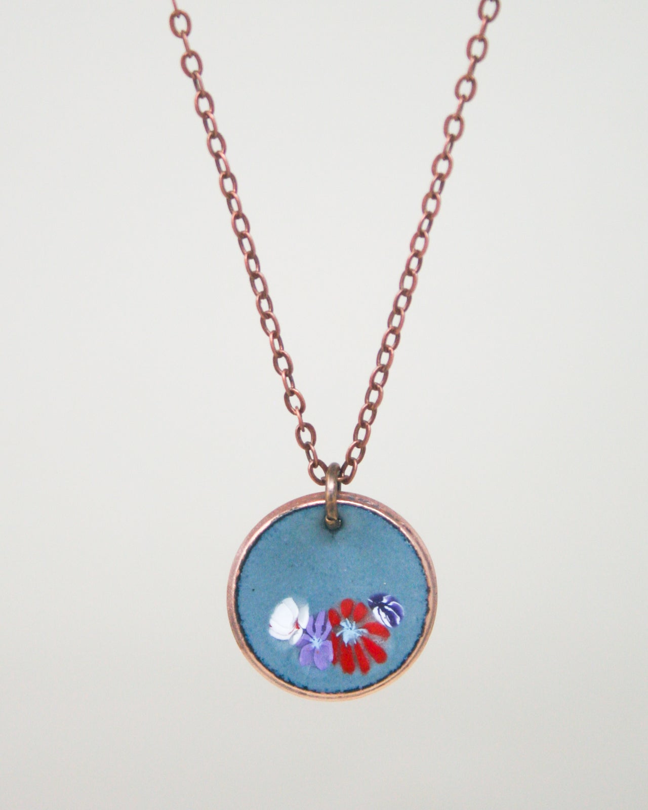 A necklace with a circular pendant featuring a floral design in blue, red, and purple colors.