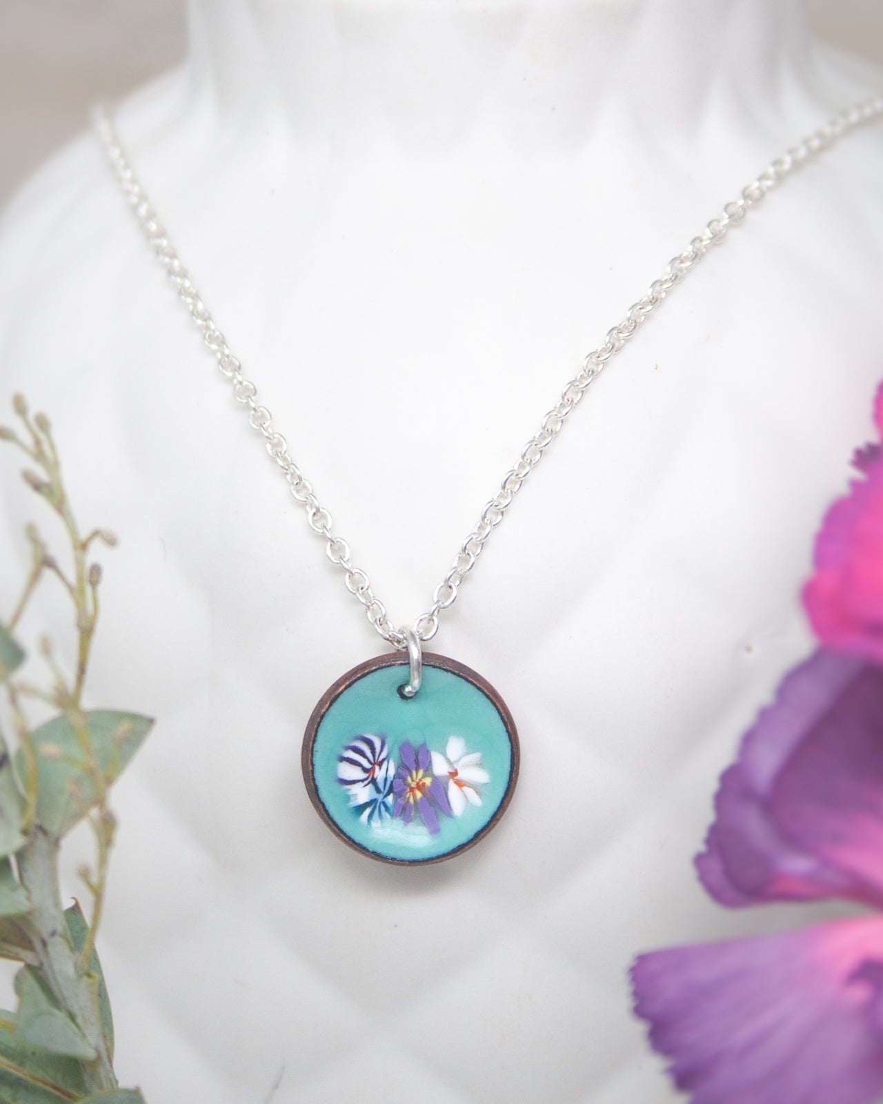 A necklace with a circular pendant featuring a floral design in turquoise and purple colors.