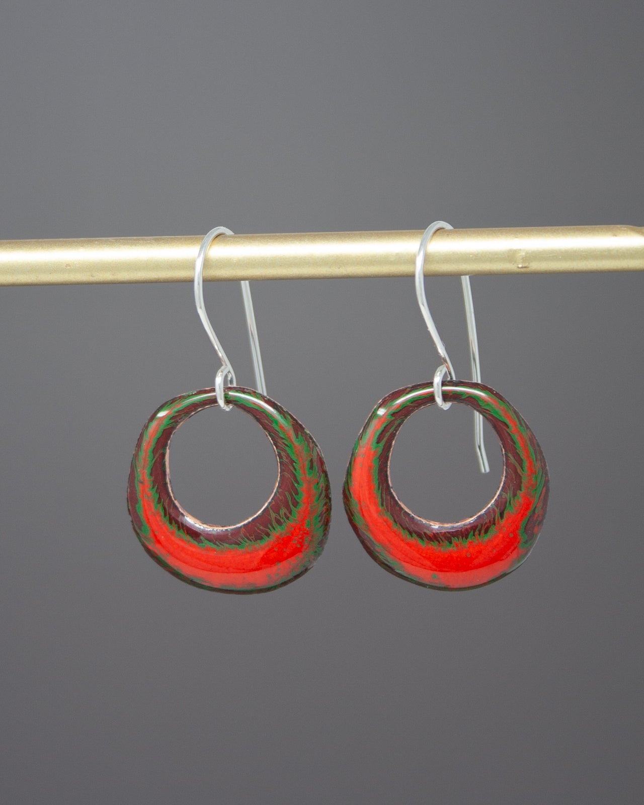 A pair of red and green hoop earrings hanging from a gold bar.