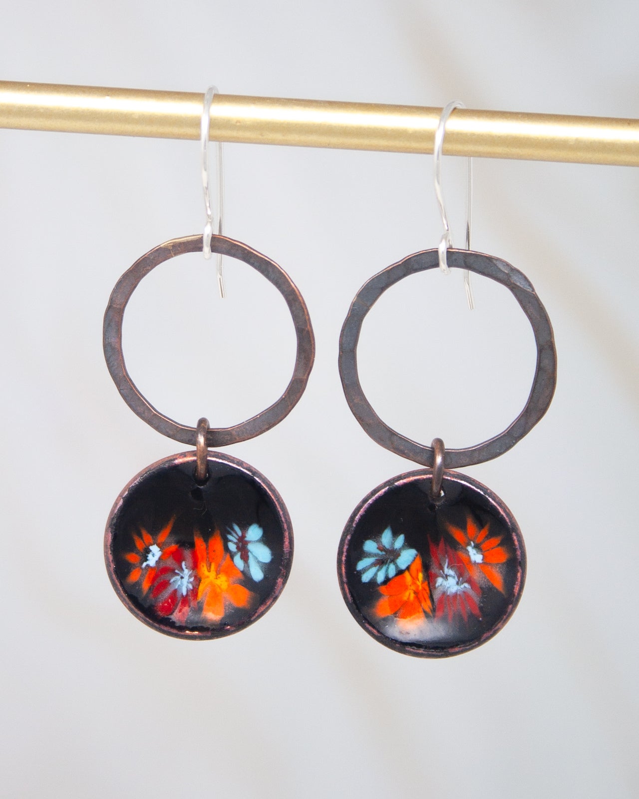 A pair of earrings with a floral design on the circular pendants, hanging from a gold-colored metal hook.