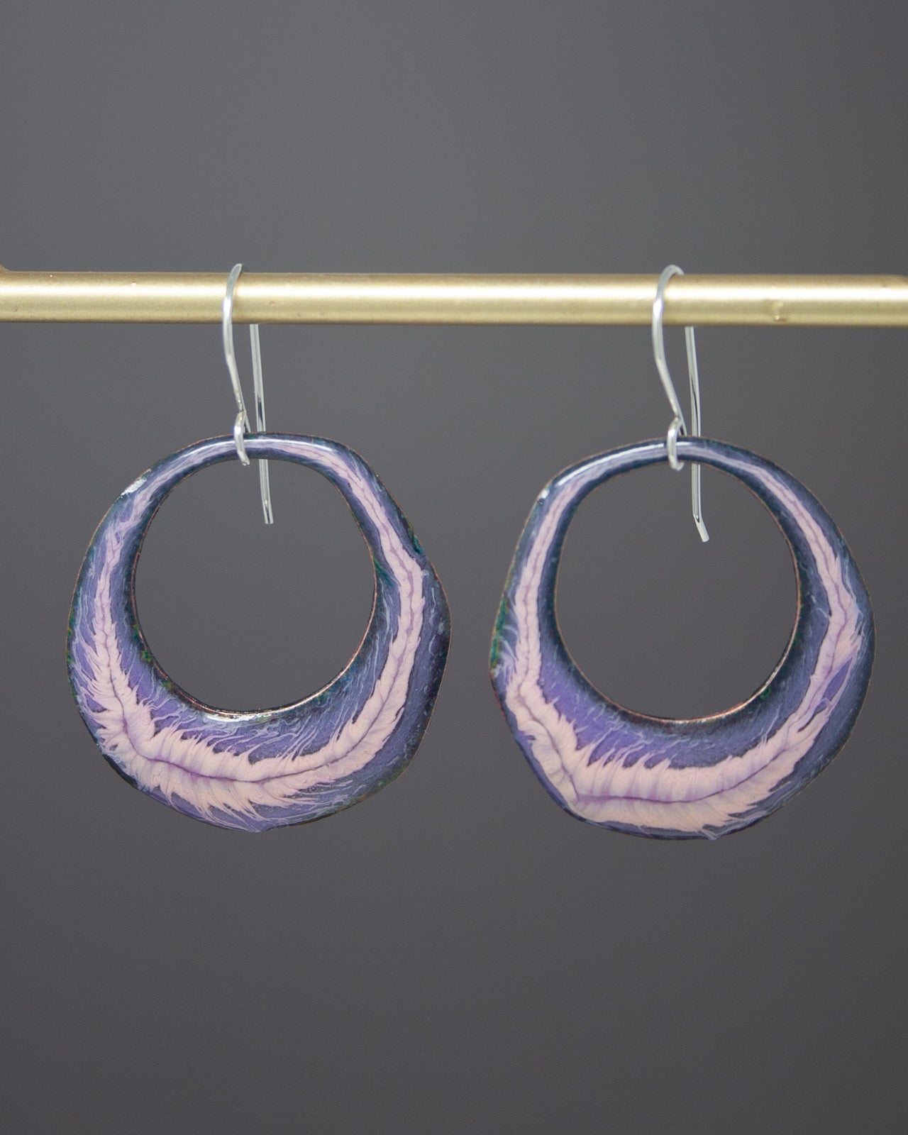A pair of earrings with a purple and white color scheme, hanging from a gold-colored metal bar.