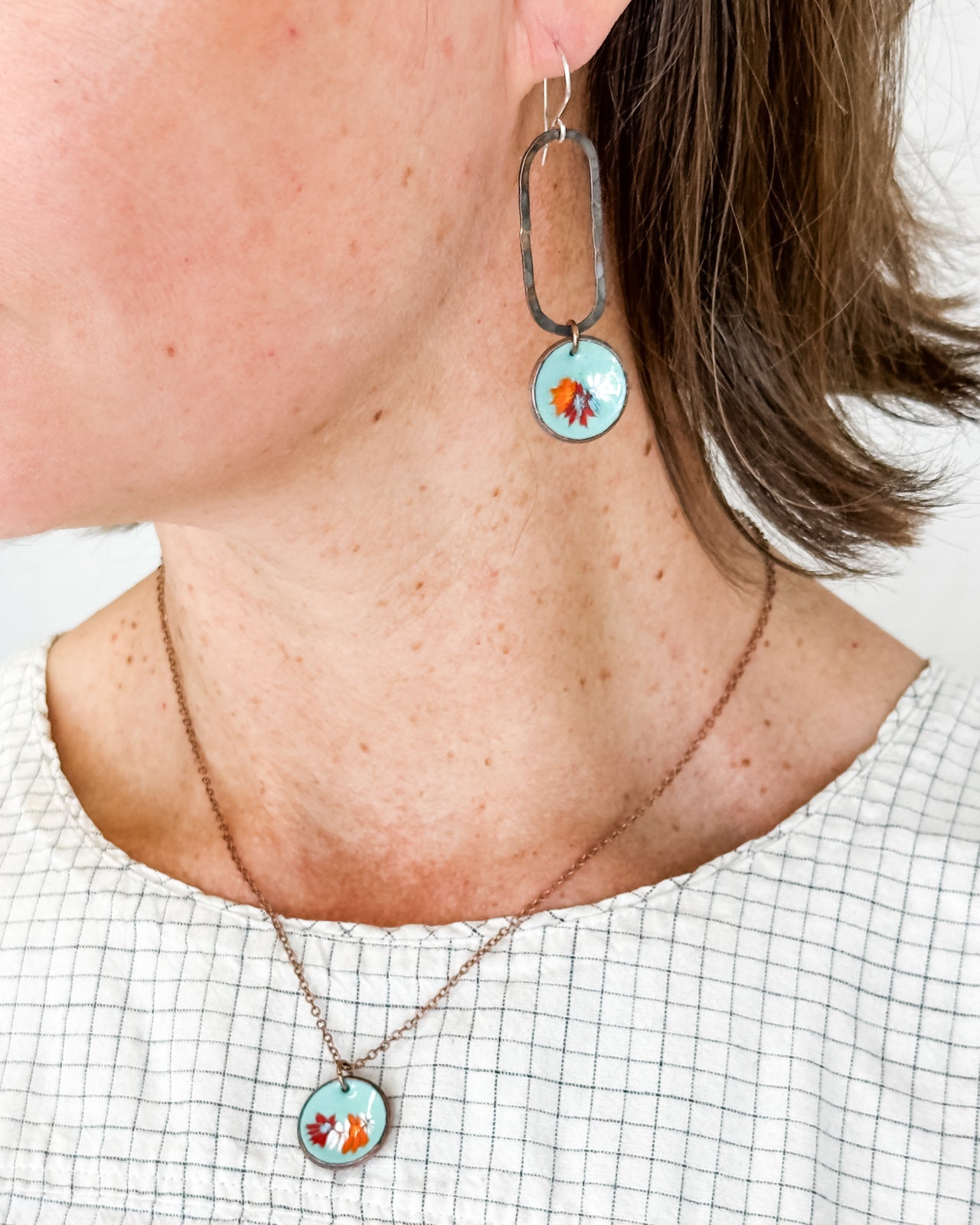 A woman wearing a necklace with a pendant and earrings with a circular design.