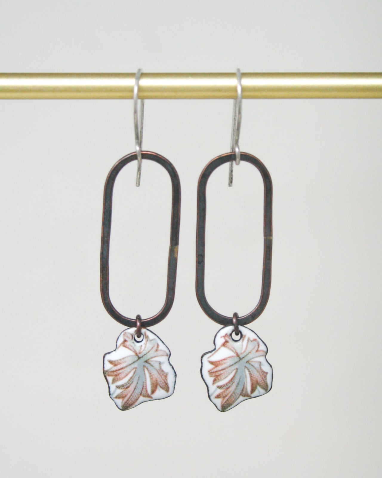 A pair of earrings with a leaf design hanging from the hooks.