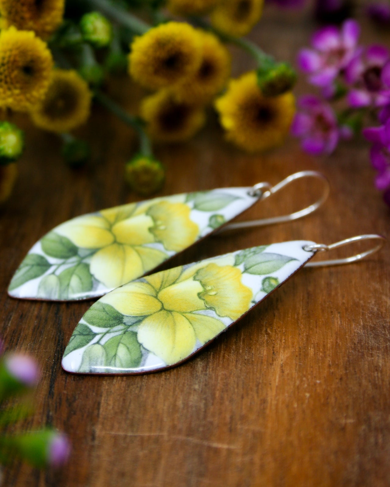 a pair of yellow and green flower earrings sitting on top of a wooden table
