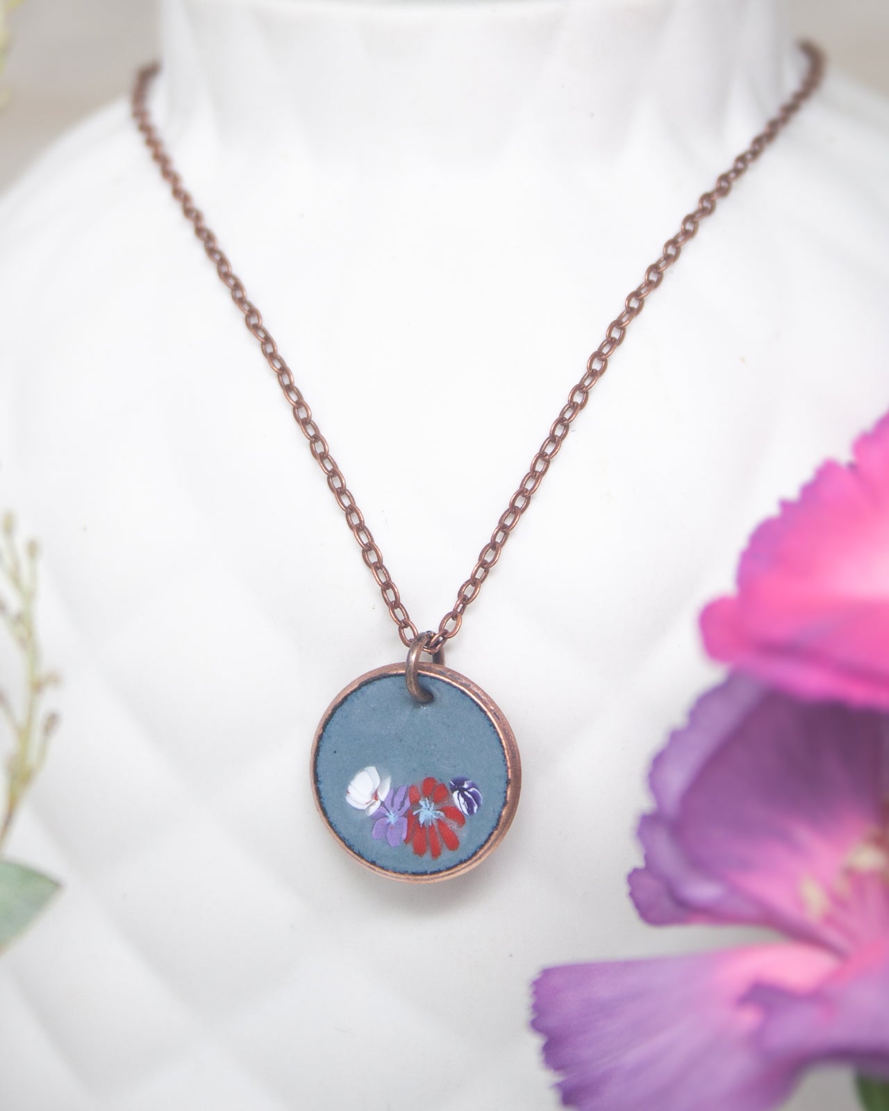 A necklace with a blue pendant featuring a floral design is displayed against a white background.