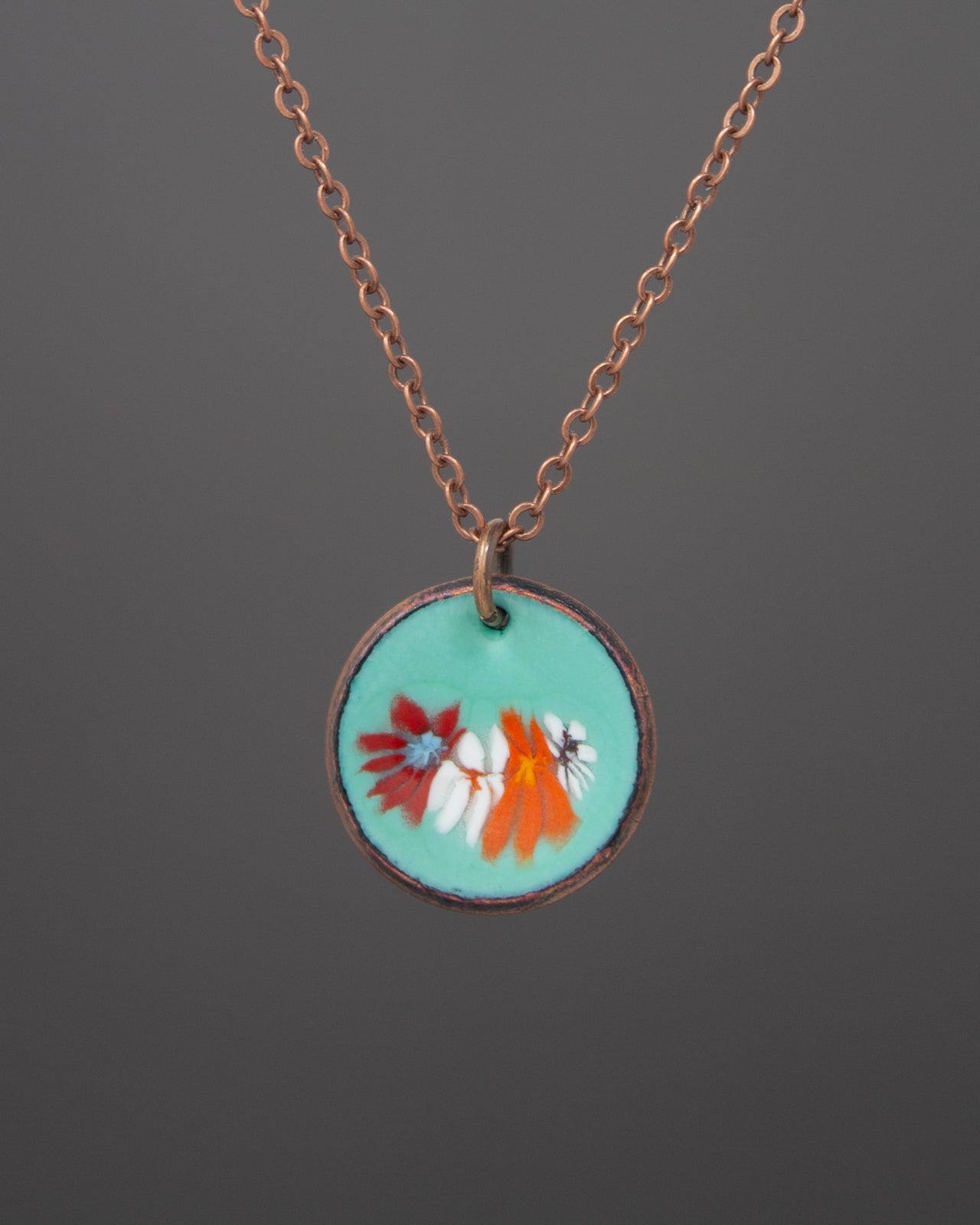 A necklace with a circular pendant featuring a floral design in turquoise and orange colors.