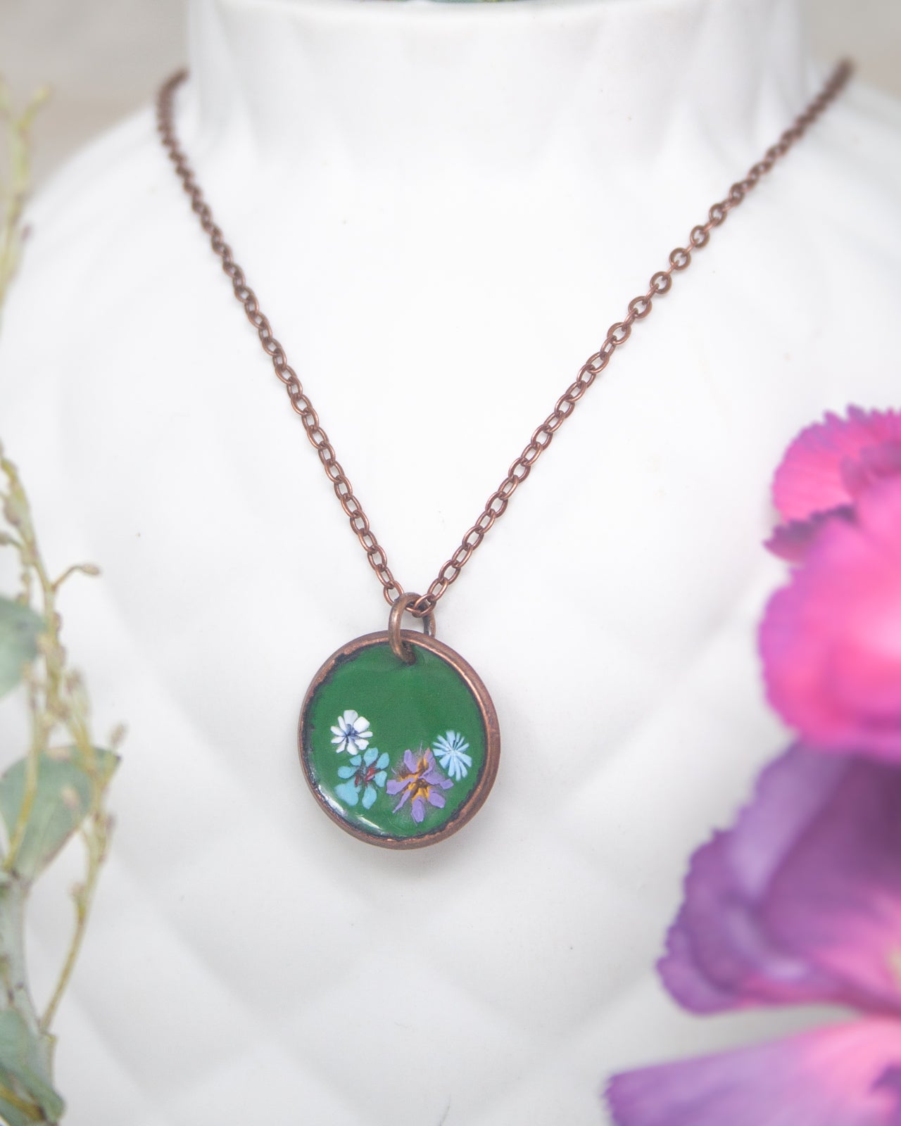 A necklace with a green pendant featuring colorful flowers is displayed against a white background.