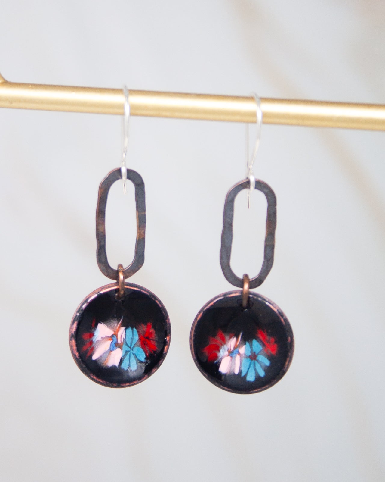 A pair of black earrings with circular designs featuring colorful floral patterns.