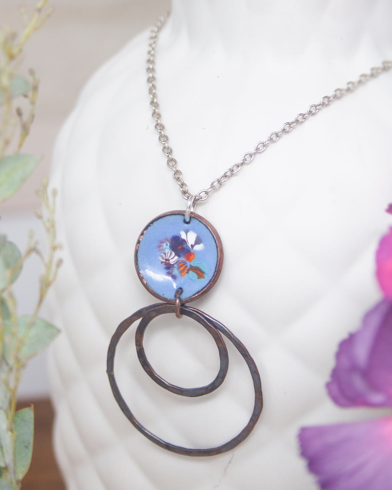 A necklace with a circular pendant featuring a floral design, hanging from a silver chain.