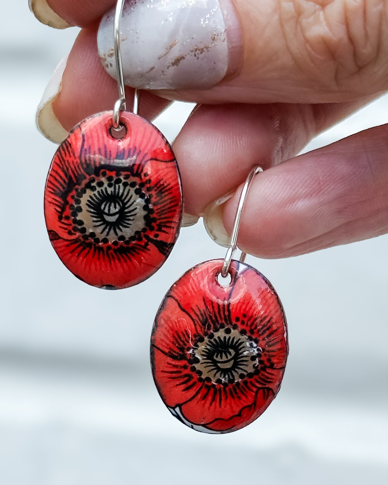 A hand holding a pair of red earrings with a floral design.