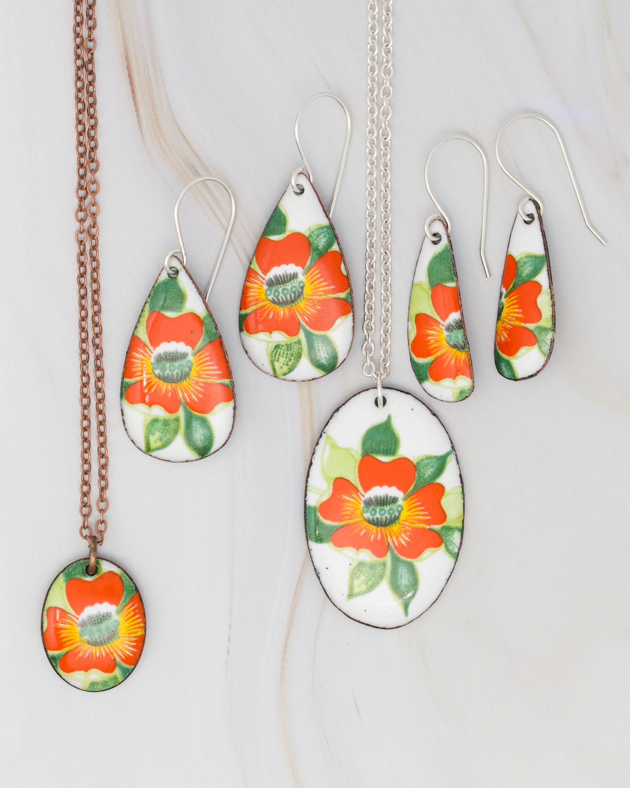 a collection of colorful floral-patterned earrings and a necklace against a white marble background.