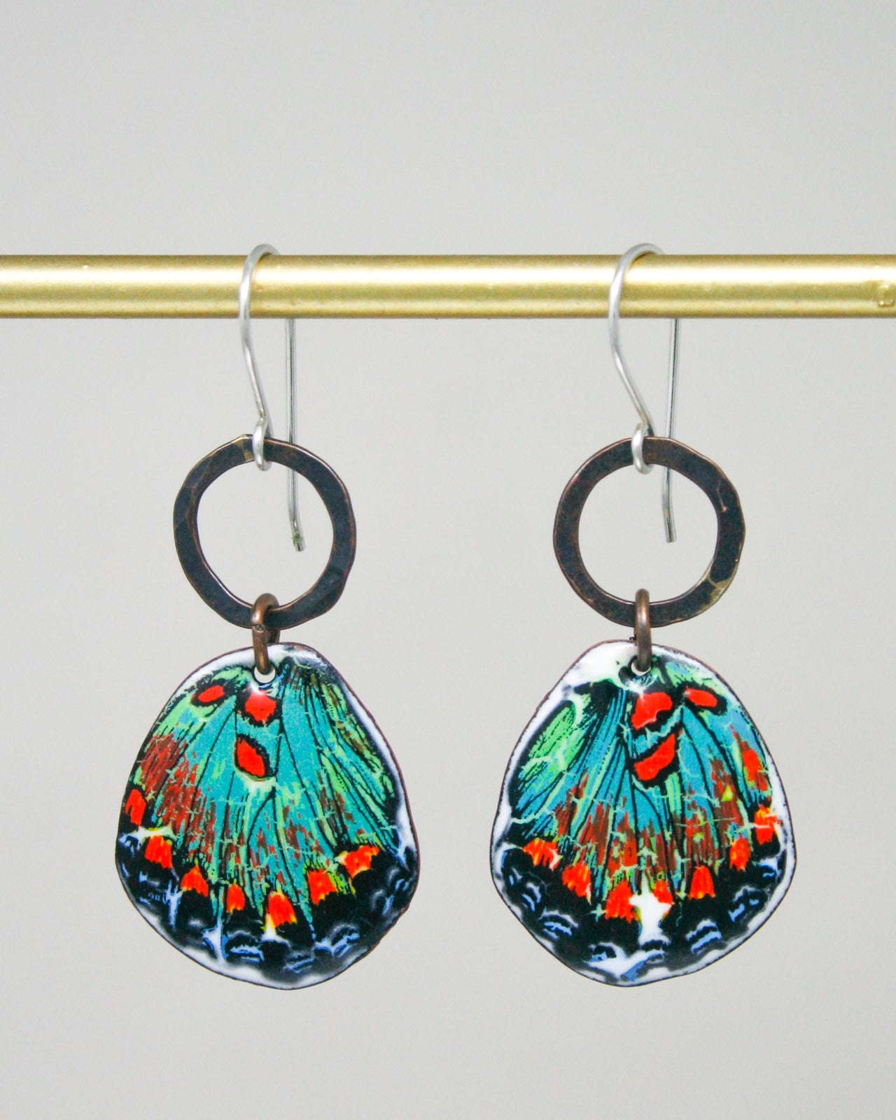 A pair of colorful earrings with butterfly wing designs hanging from a gold-colored metal hook.