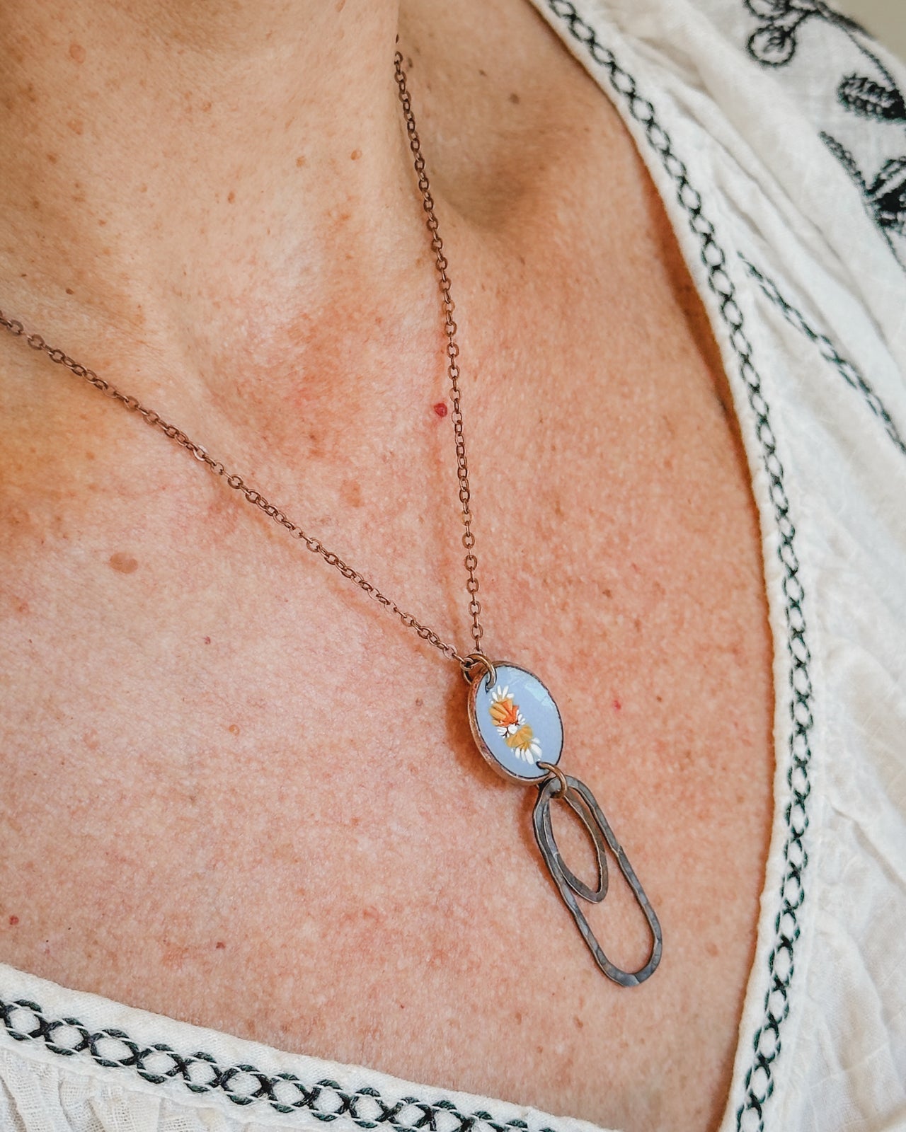 A close-up view of a woman's neck and chest area, showing a necklace with a pendant featuring a floral design.