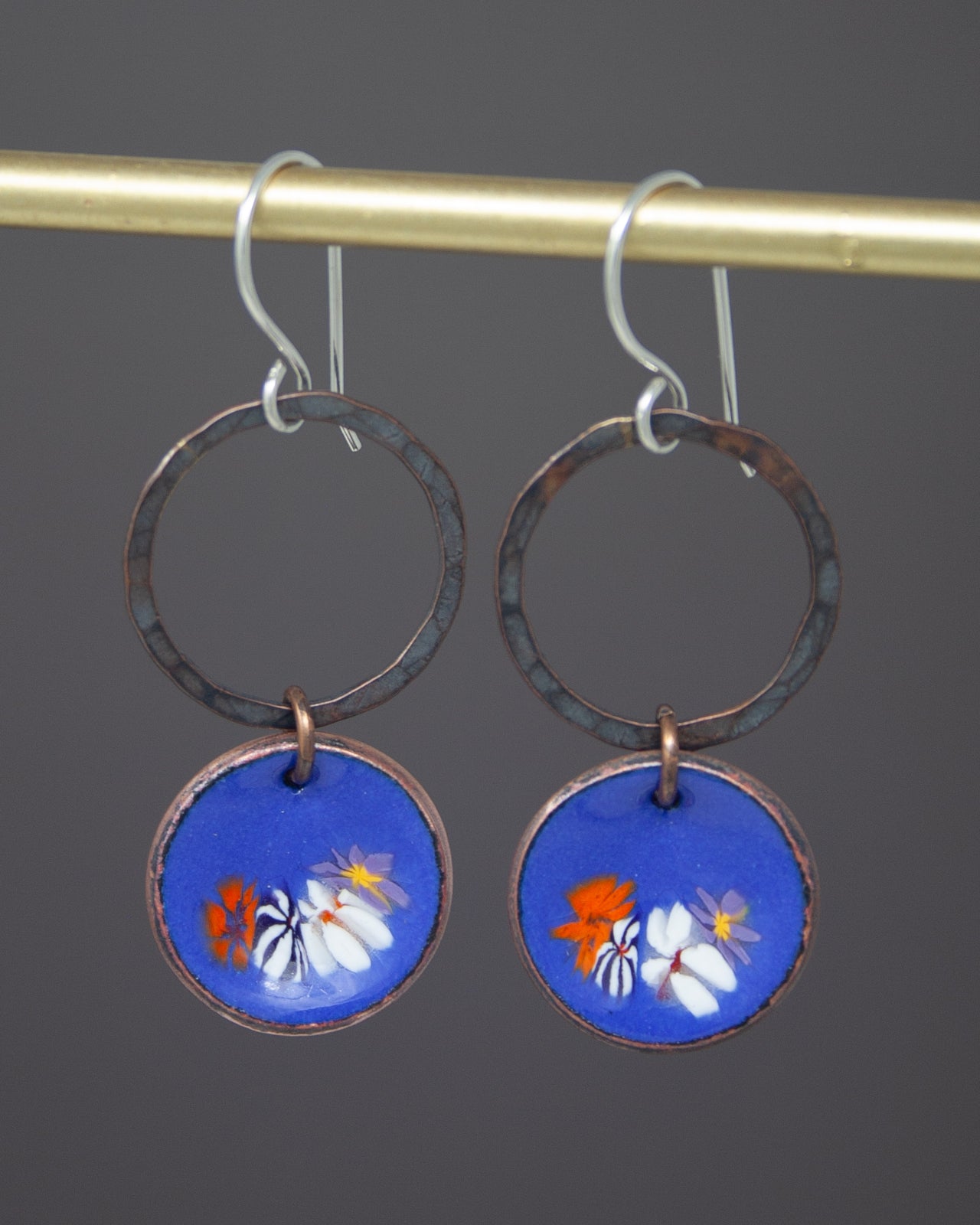 A pair of earrings with blue and copper-colored circular pendants featuring a floral design.