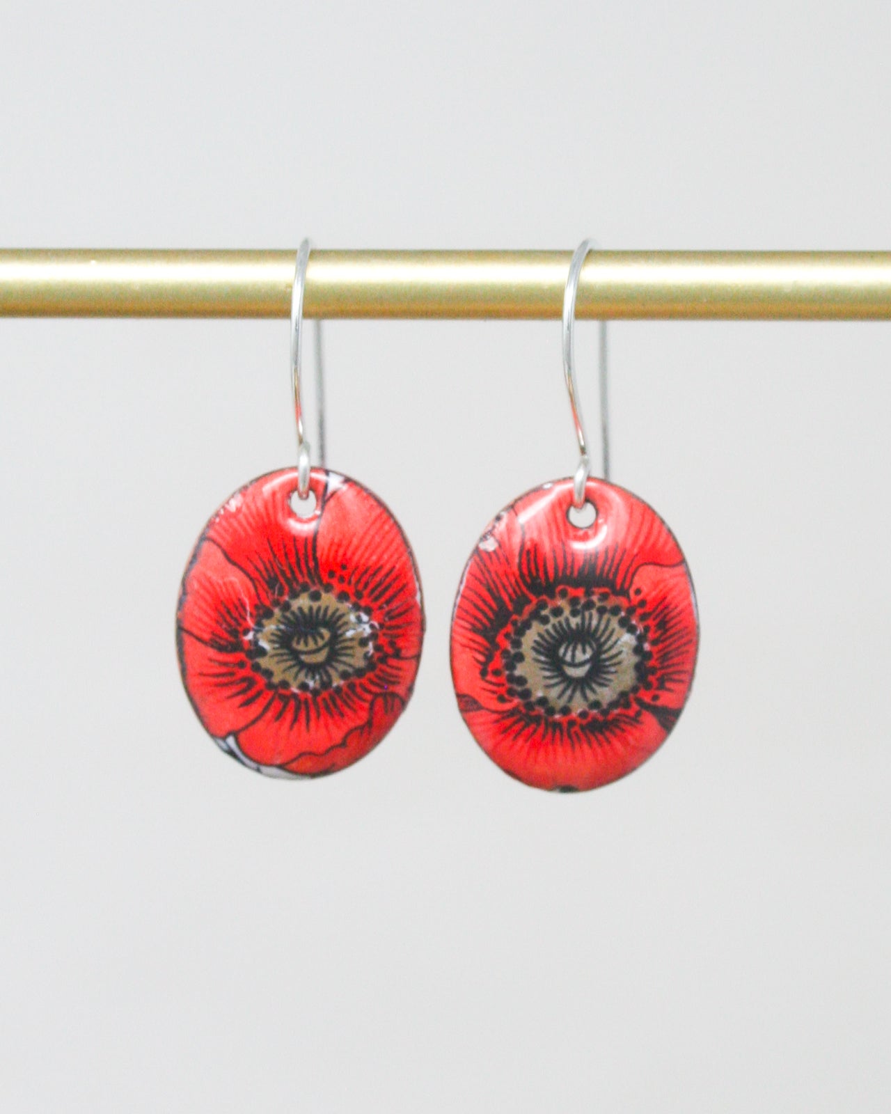 A pair of red earrings with black floral designs hanging from a gold bar.