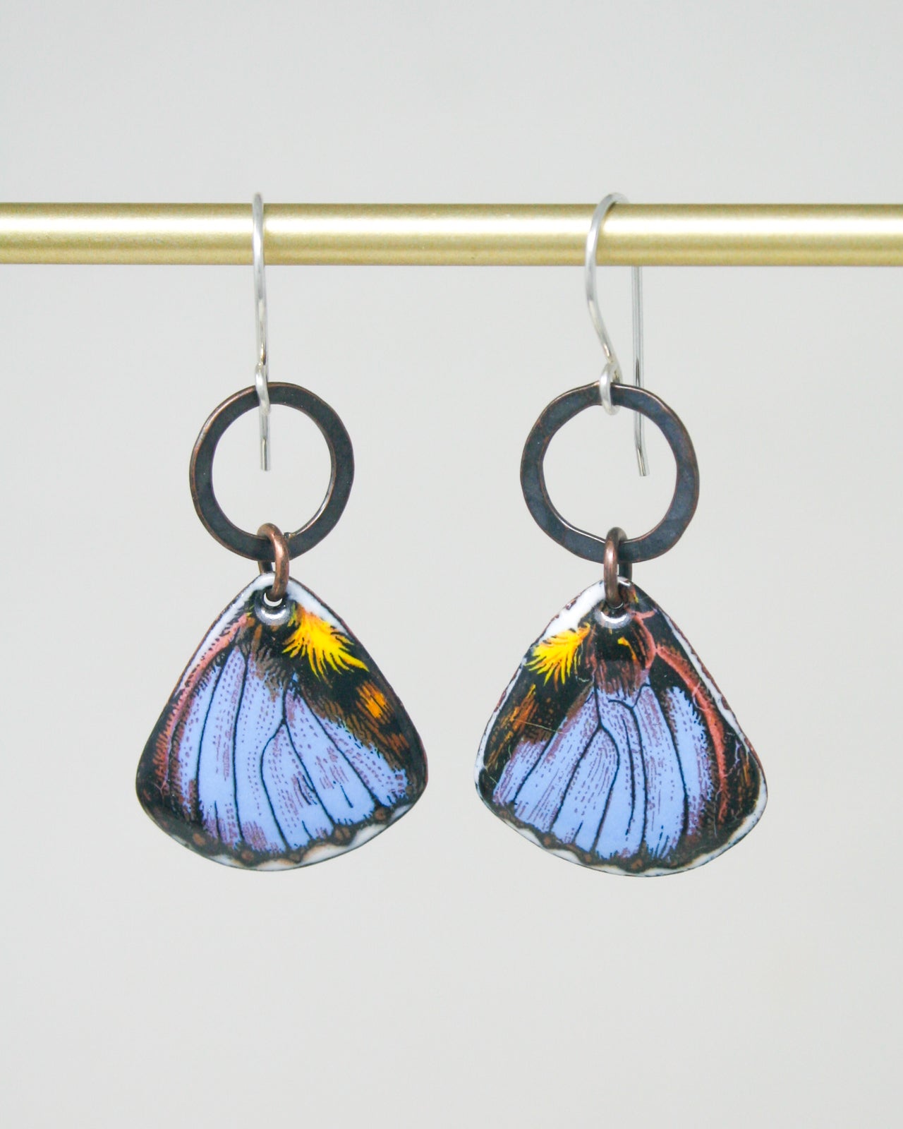 A pair of earrings with butterfly wing designs, hanging from a gold-colored metal hook.