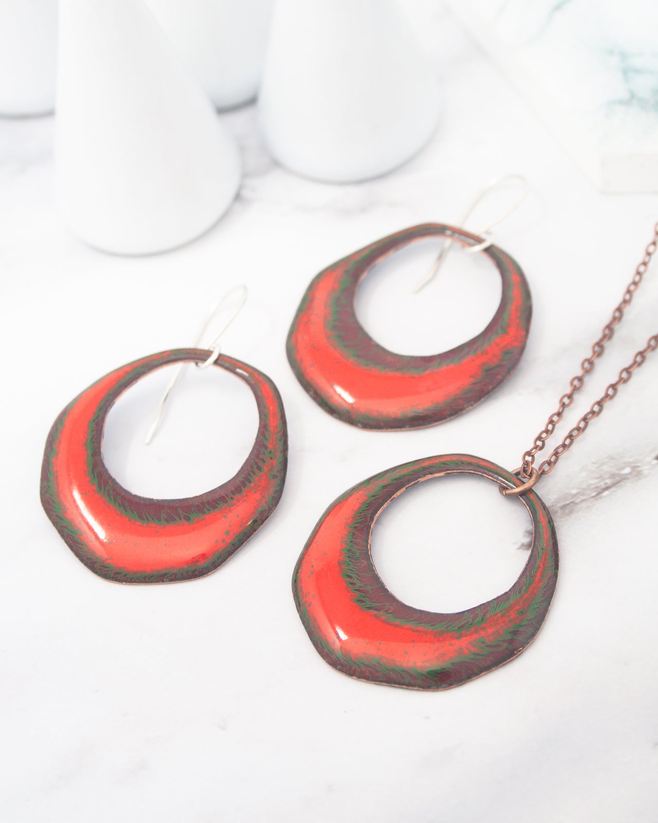 a pair of red and green metal earrings and a necklace with a chain, arranged on a white surface.