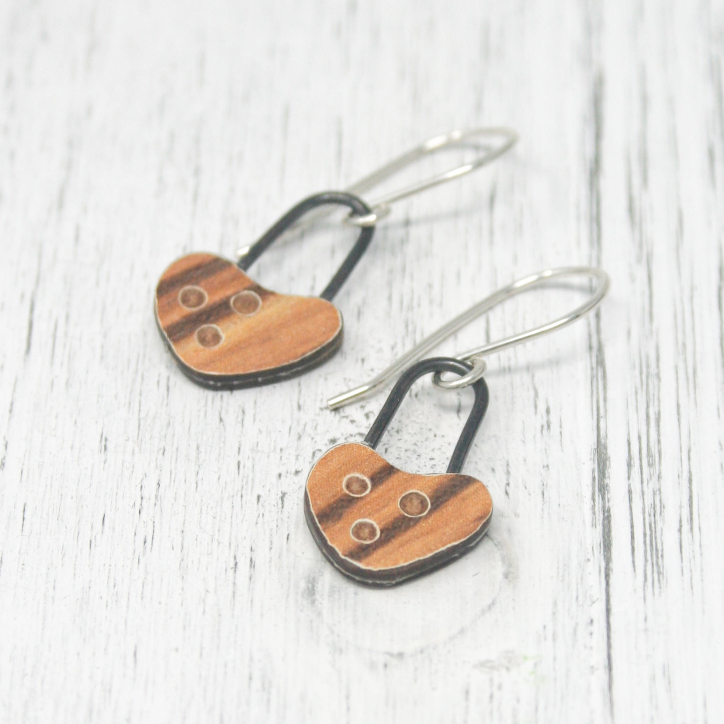 A pair of wooden heart-shaped earrings with metal hooks, resting on a white wooden surface.