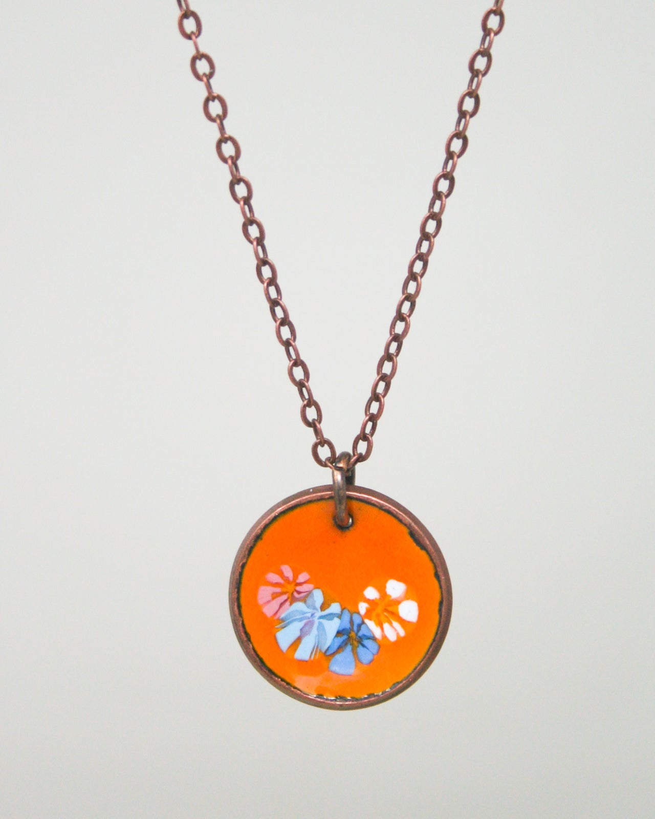 A necklace with a circular pendant featuring a floral design in orange and blue colors.