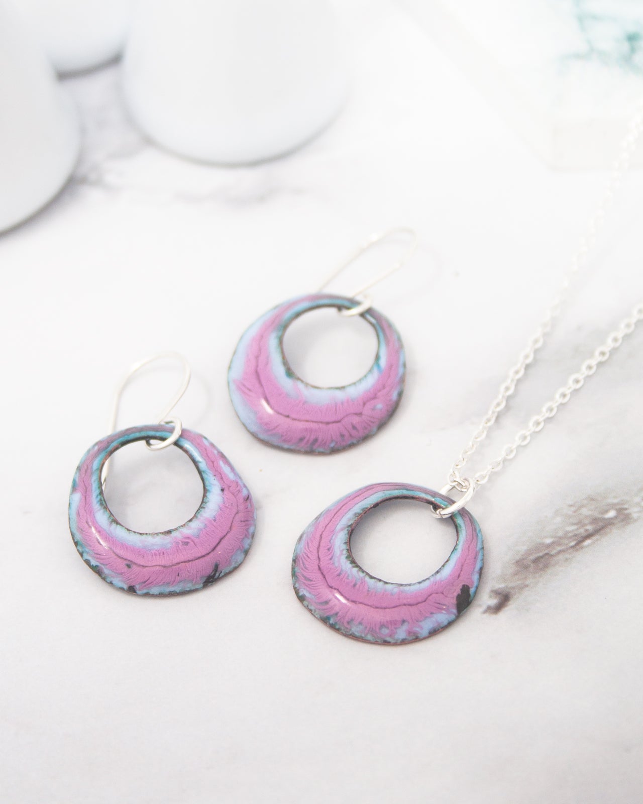 a pair of earrings and a necklace with a pink and blue color scheme, placed on a marble surface.