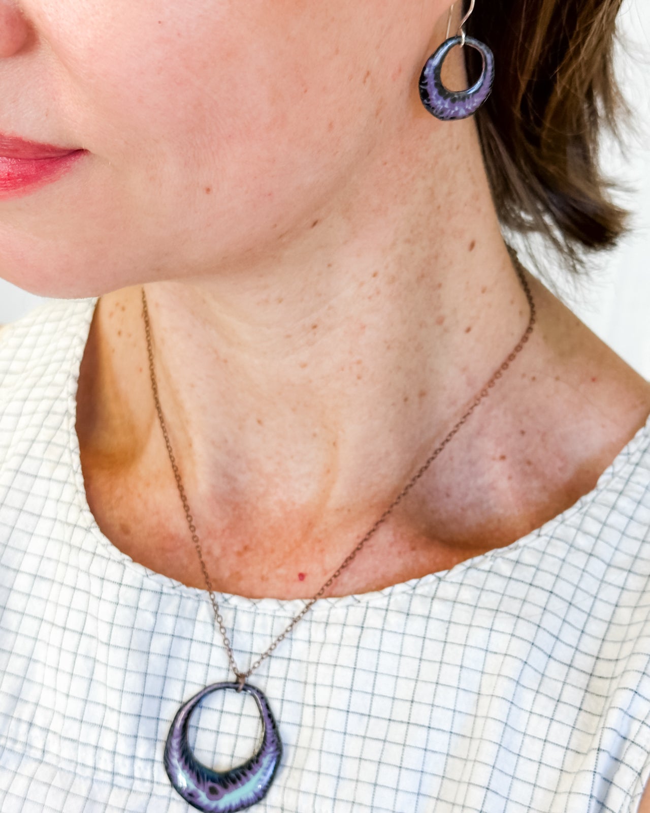 A woman wearing a necklace with a pendant and earrings is shown in the image.