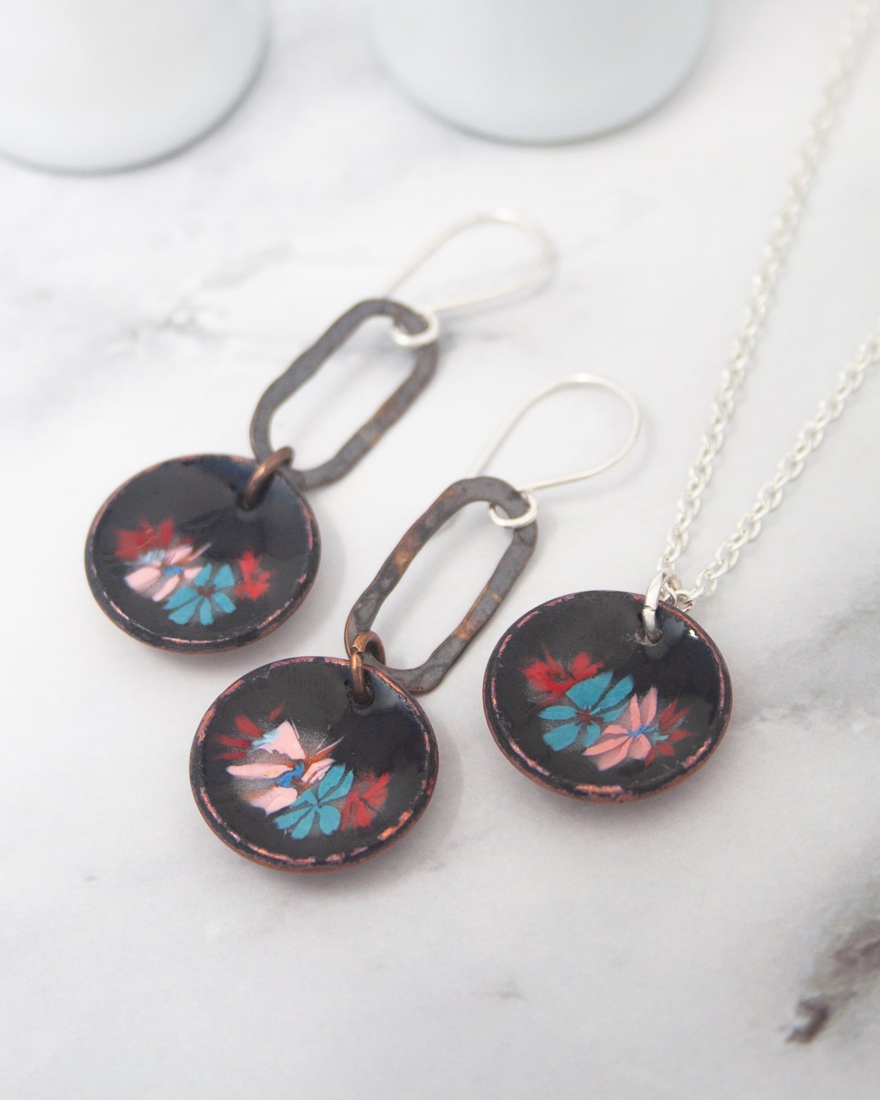 a pair of earrings and a necklace with floral designs on a marble surface.