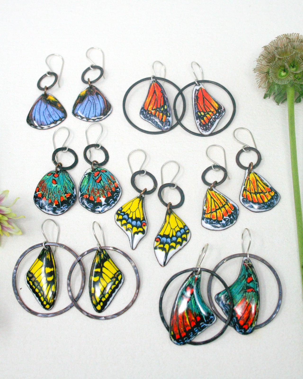 a collection of colorful butterfly-themed earrings, including various designs and colors such as blue, orange, yellow, green, and red. The earrings are arranged in a visually appealing manner, showcasing the intricate details and vibrant colors of the butterfly motifs.