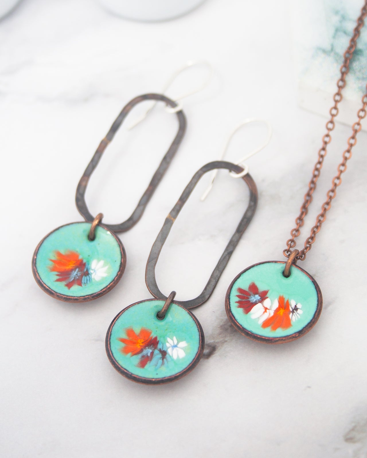 a pair of earrings and a necklace with floral designs on them, placed on a marble surface.