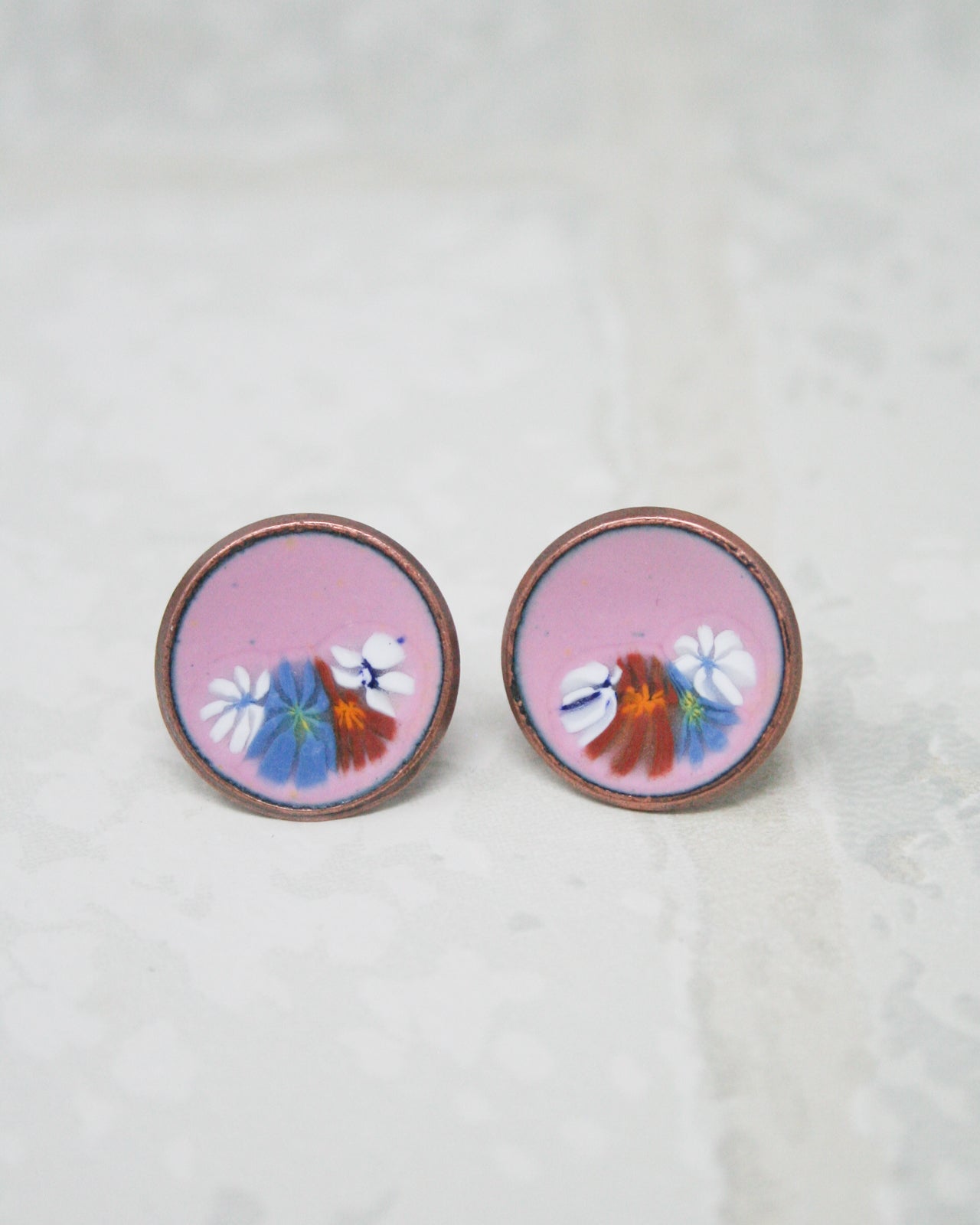 two circular earrings with a floral design, including white and orange flowers, on a light-colored background.