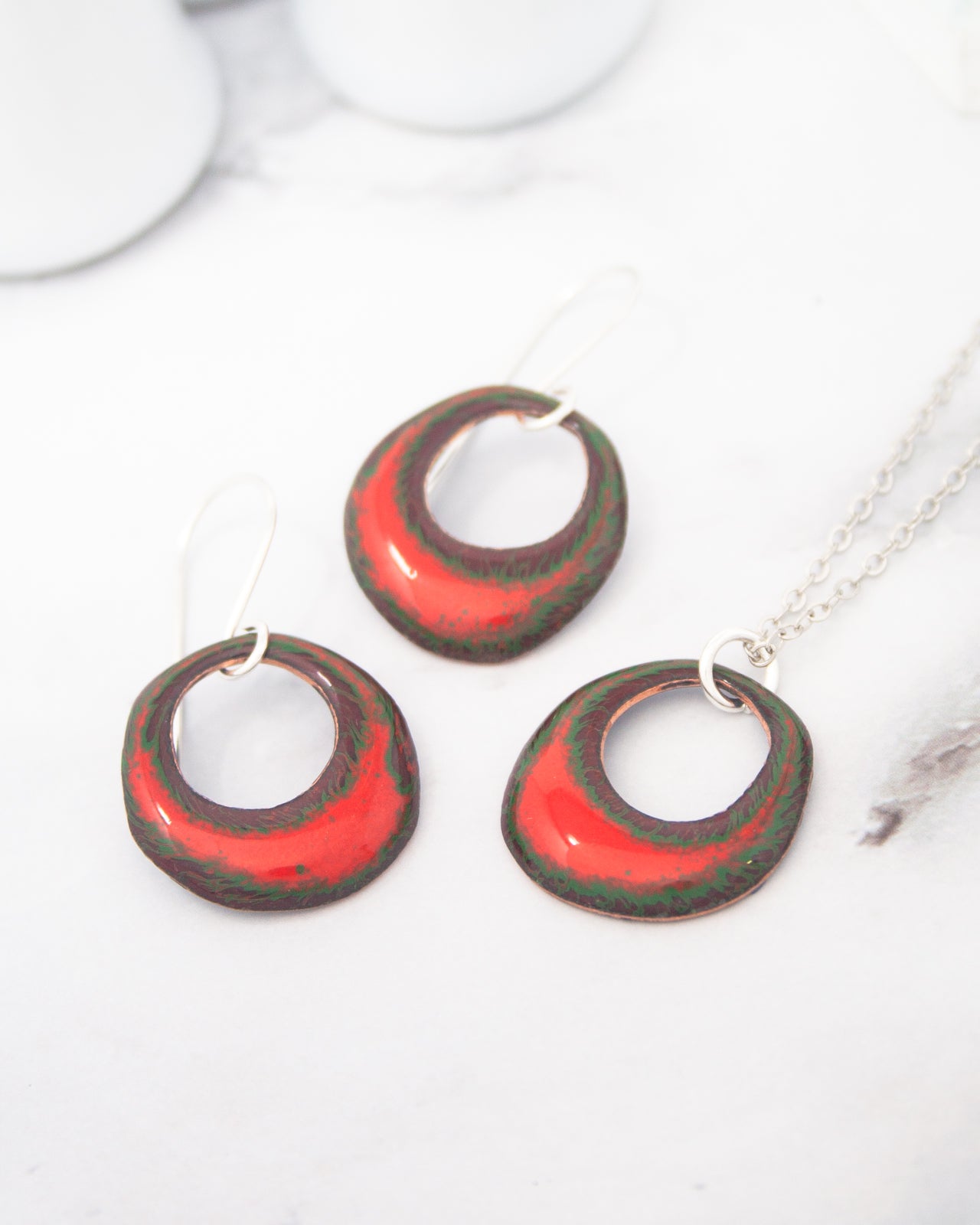 a pair of red and green earrings with a metallic appearance, placed on a white surface.