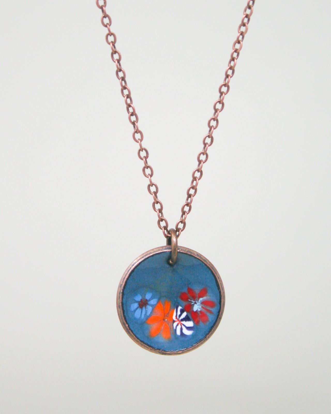 A necklace with a circular pendant featuring a floral design in blue, orange, and red colors.