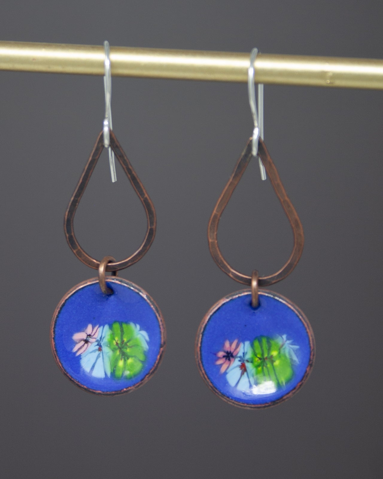 A pair of earrings with a blue circular design featuring a floral pattern, hanging from a gold-colored metal hook.