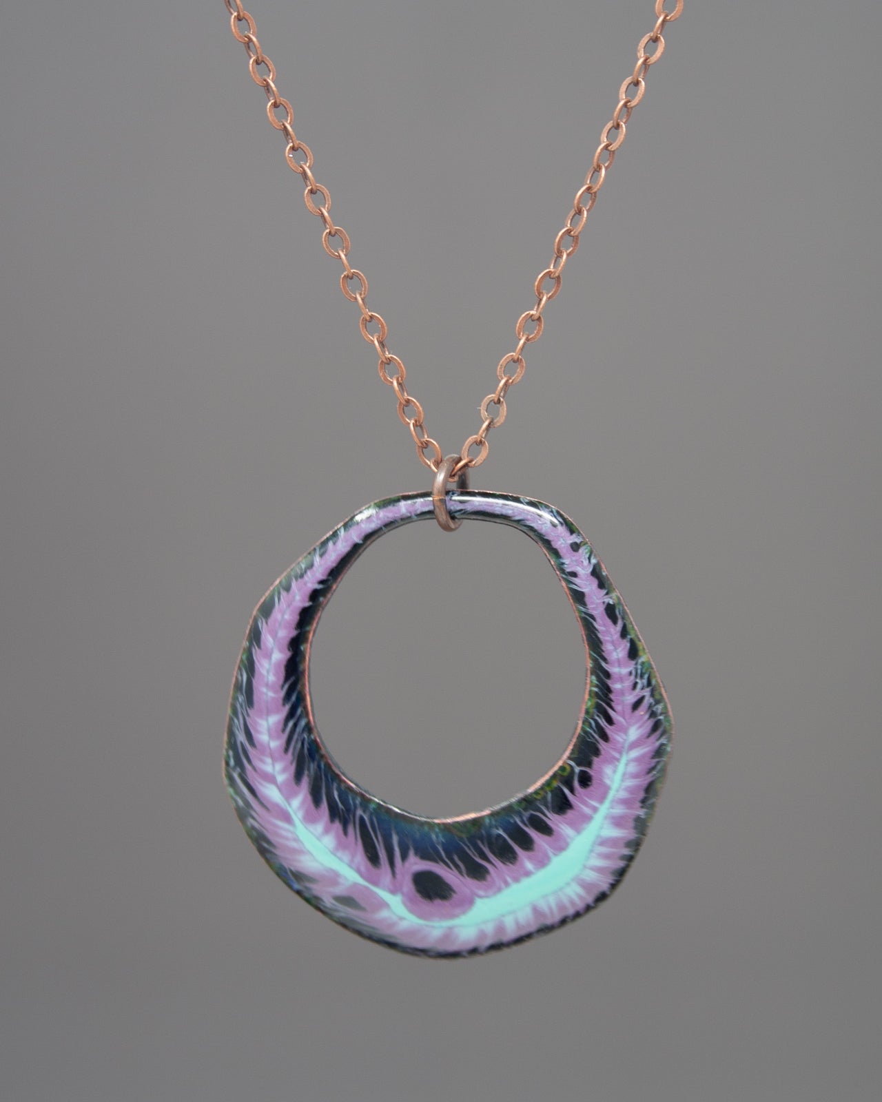 A necklace with a circular pendant featuring a floral design in shades of purple and green.