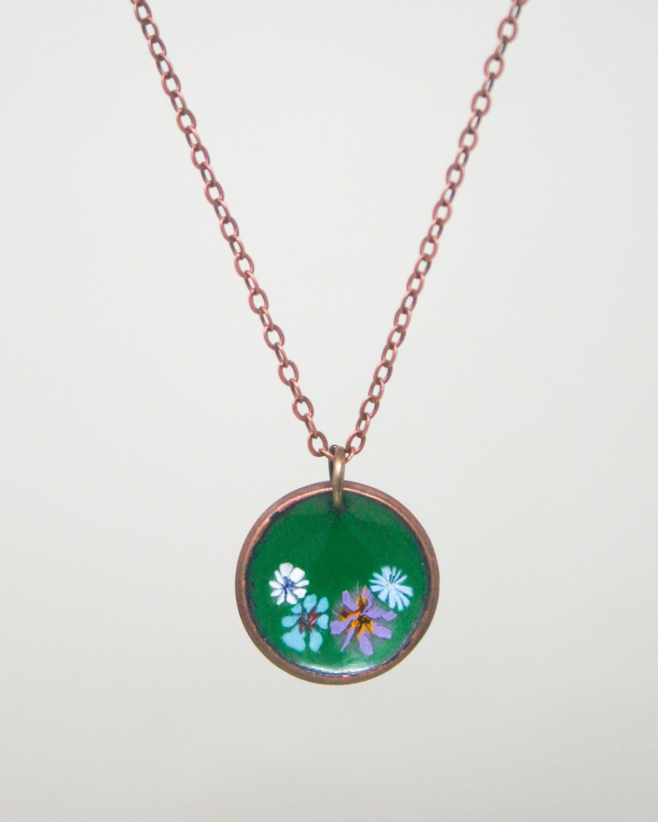A necklace with a circular pendant featuring a green background and colorful flowers.