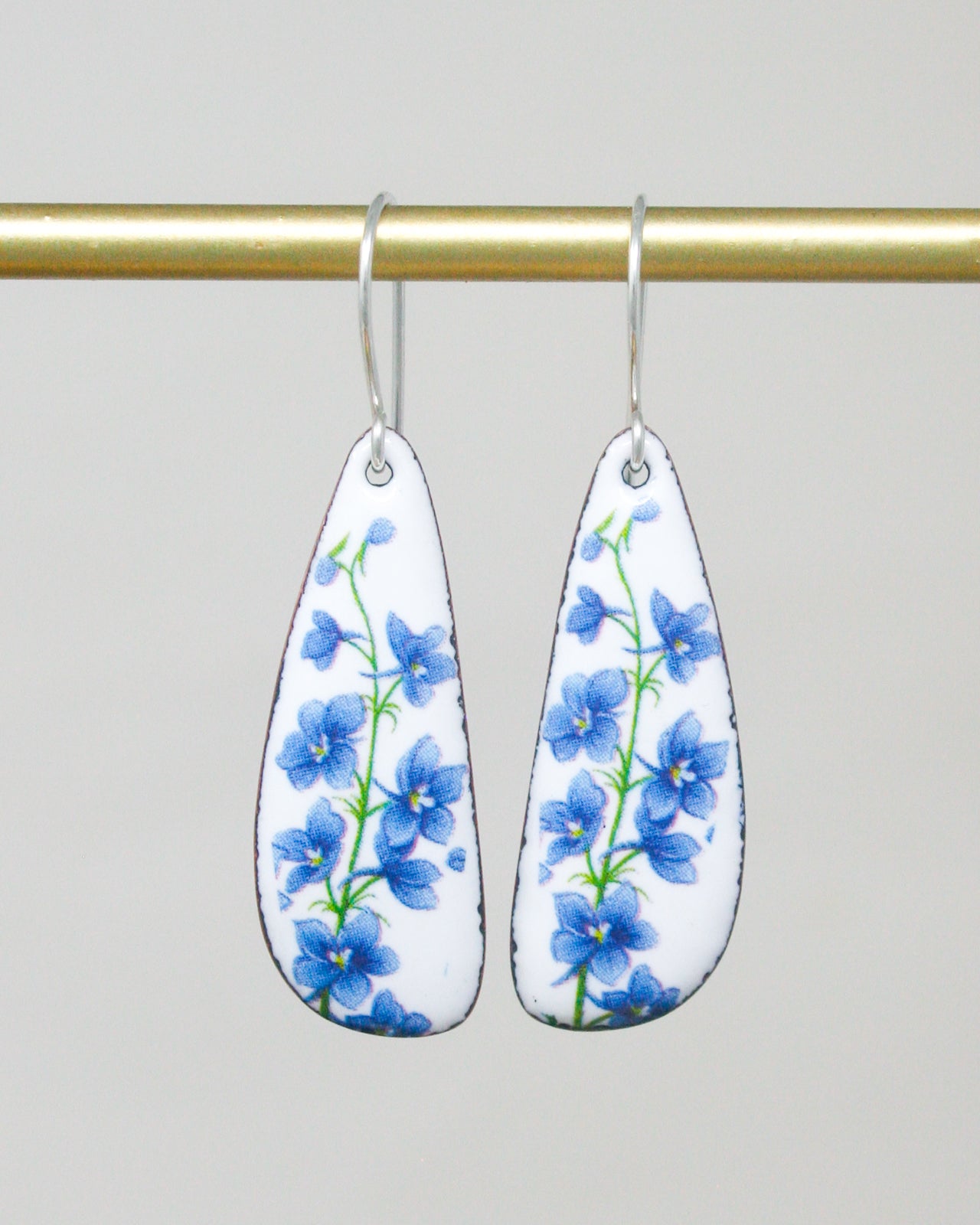 A pair of earrings with blue flowers on a white background, hanging from a gold bar.