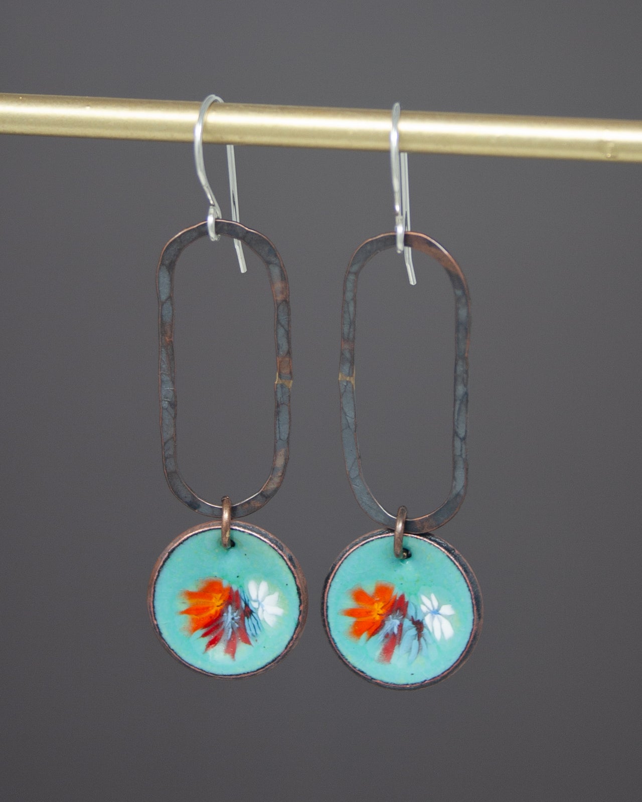 A pair of earrings with a floral design on the circular pendants, hanging from a gold-colored metal hook.