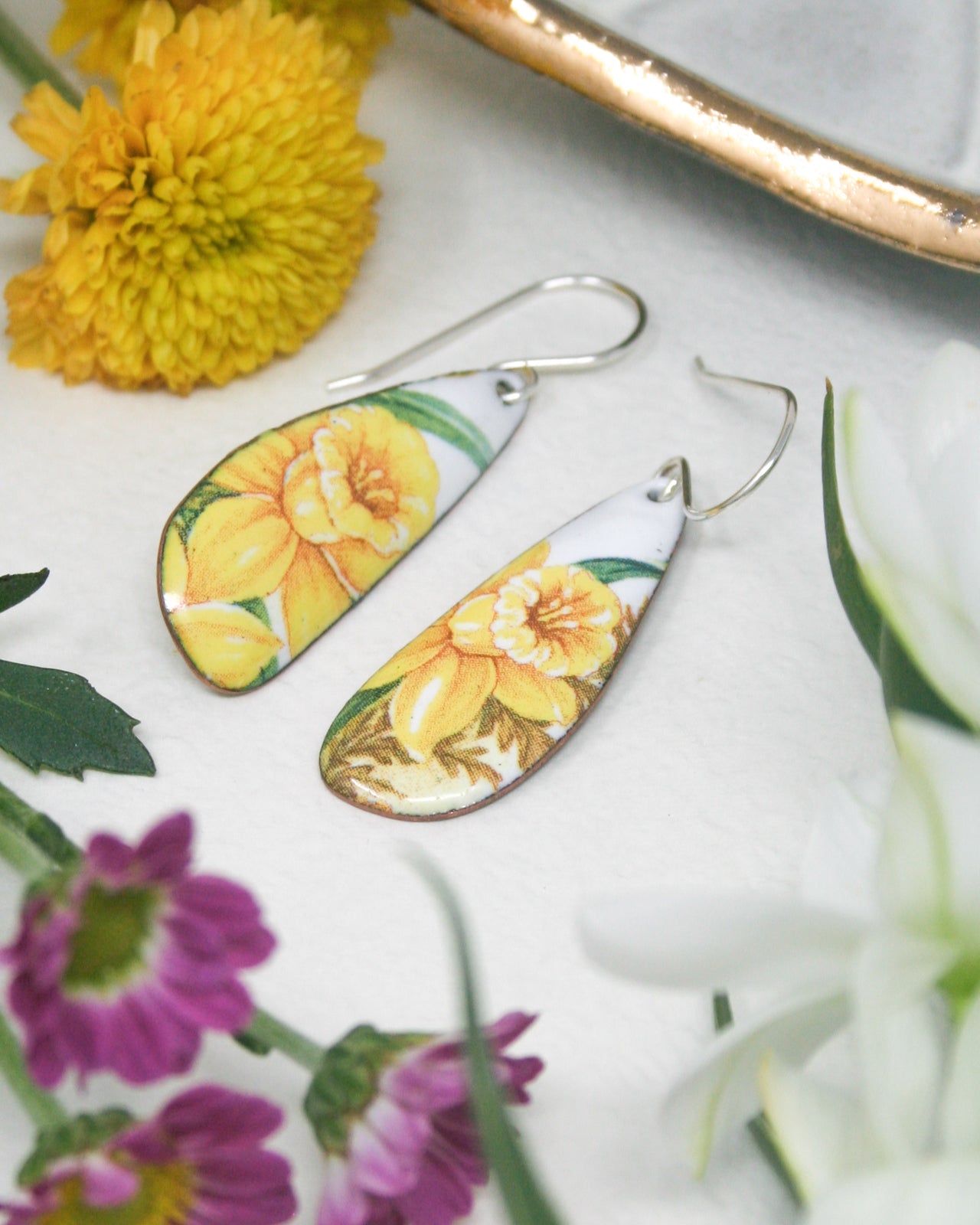 a close up of a pair of earrings on a table with flowers
